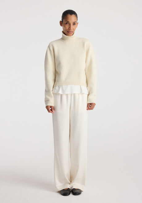 Woman wearing cream-colored relaxed fit satin trousers paired with a light sweater and black shoes against a plain white background, showcasing Relaxed fit satin trousers | cream.