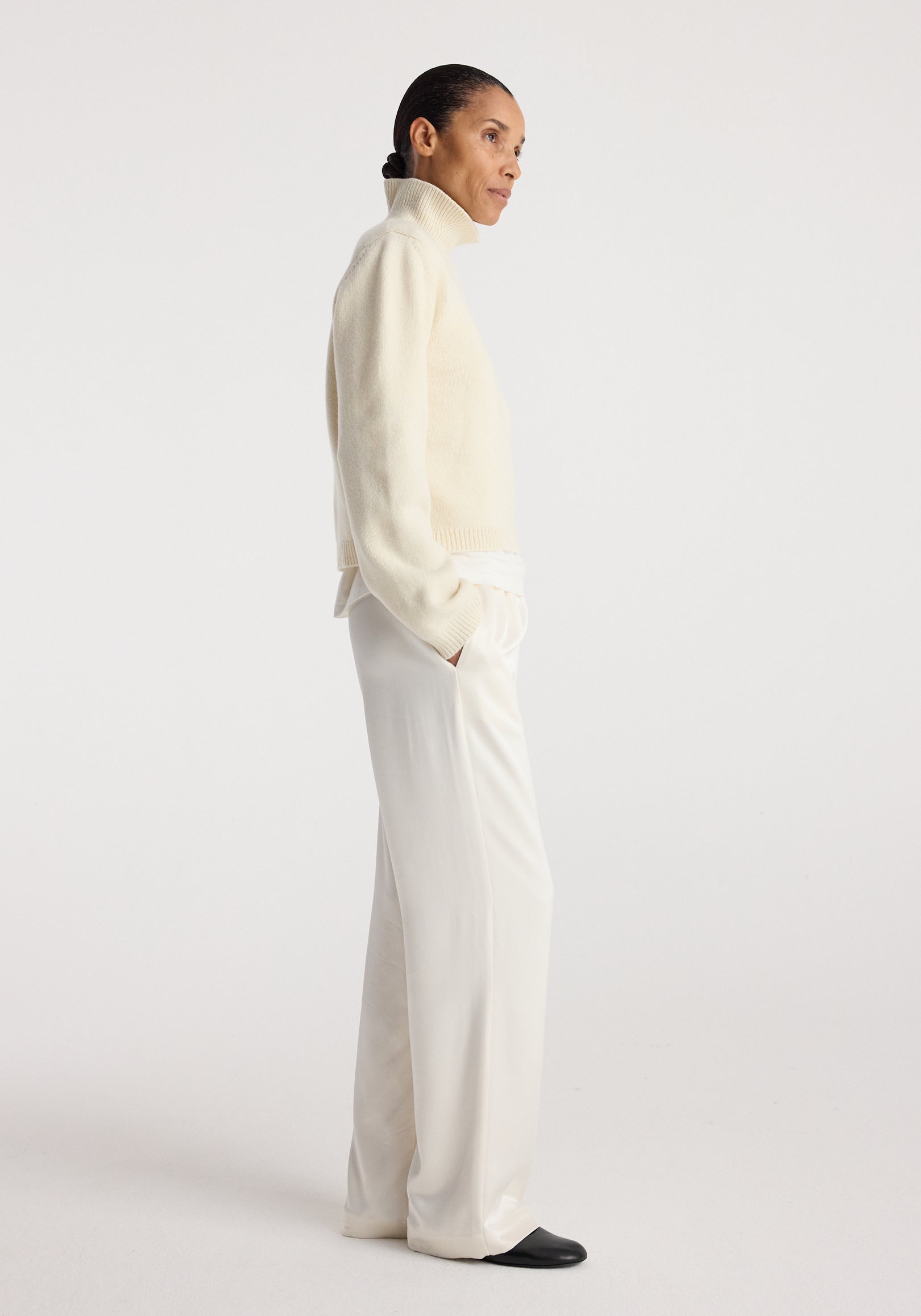 Woman wearing cream high-neck sweater paired with relaxed fit satin trousers | cream and black shoes against a plain white background.