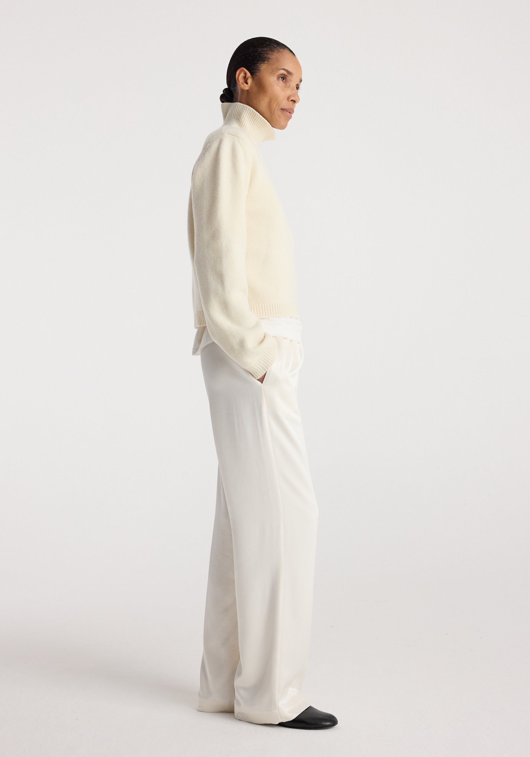 Woman wearing cream high-neck sweater paired with relaxed fit satin trousers | cream and black shoes against a plain white background.