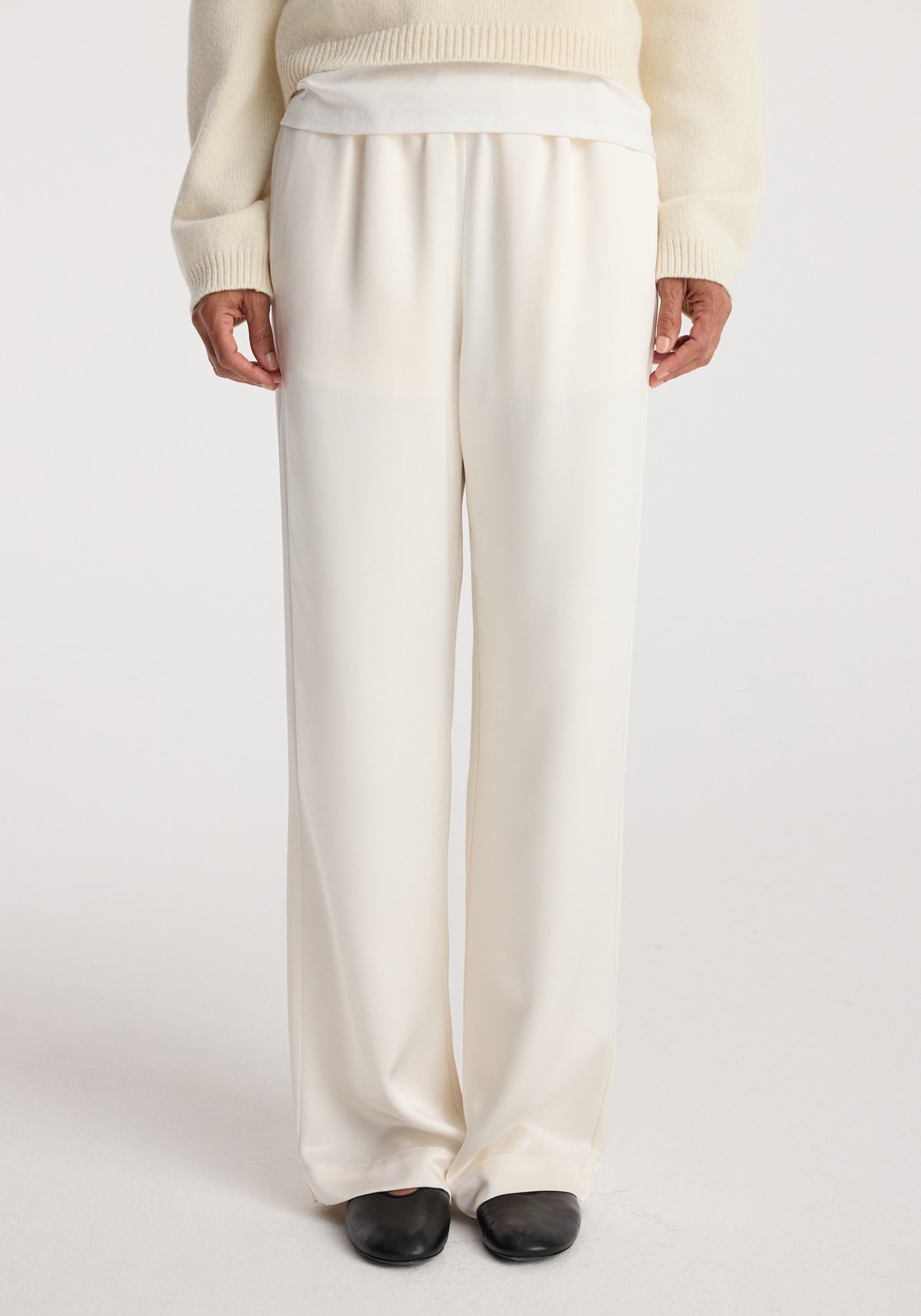 Relaxed fit satin trousers | cream shown on a model wearing a cream sweater and black shoes, highlighting the smooth texture and loose silhouette of the pants.