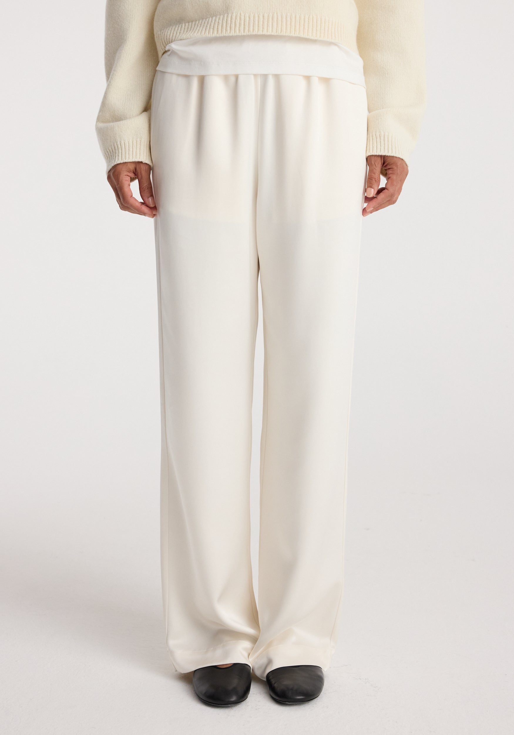 Relaxed fit satin trousers | cream shown on a model wearing a cream sweater and black shoes, highlighting the smooth texture and loose silhouette of the pants.
