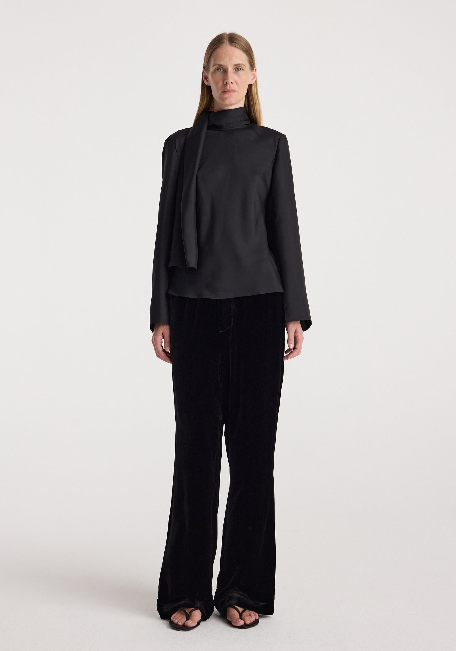 Woman wearing black long-sleeve top paired with Velvet relaxed trousers | black, standing against a plain light background in a relaxed pose.