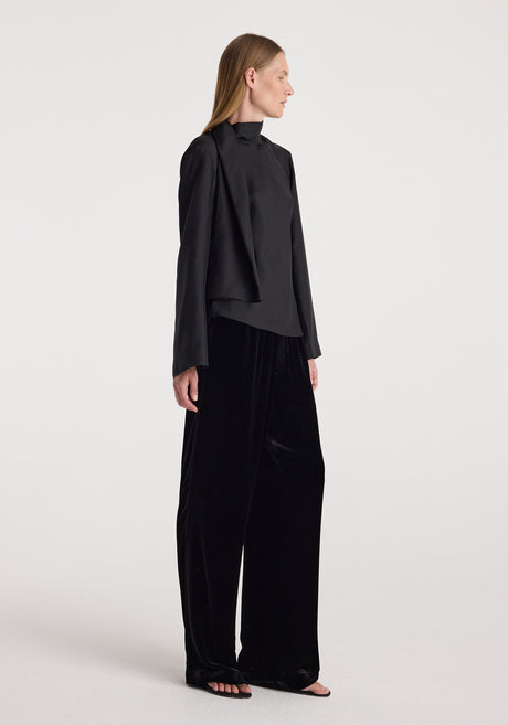 Woman wearing black long-sleeve top paired with Velvet relaxed trousers | black, standing against a plain light background in a relaxed pose.