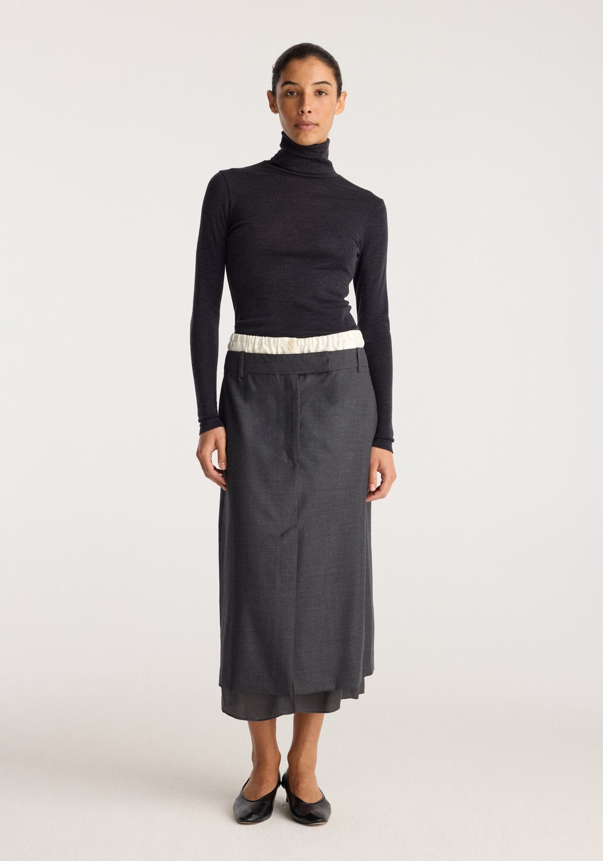 Boxer detailed skirt | dark grey melange worn by a model with a black turtleneck top and black flats in a studio setting
