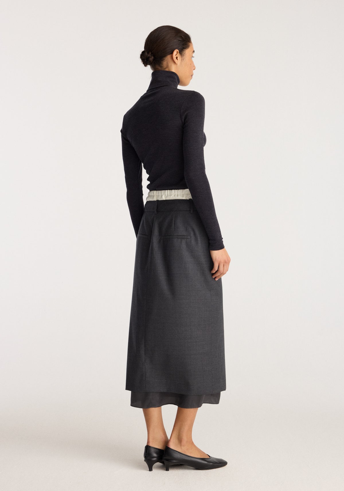 Boxer detailed skirt | dark grey melange shown from the back with a long midi silhouette and layered hem styled with a black turtleneck and shoes
