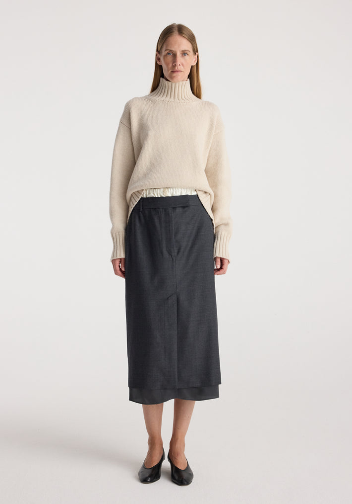 Woman wearing a light beige turtleneck sweater paired with a dark grey melange Boxer detailed skirt | dark grey melange, standing against a plain white background.