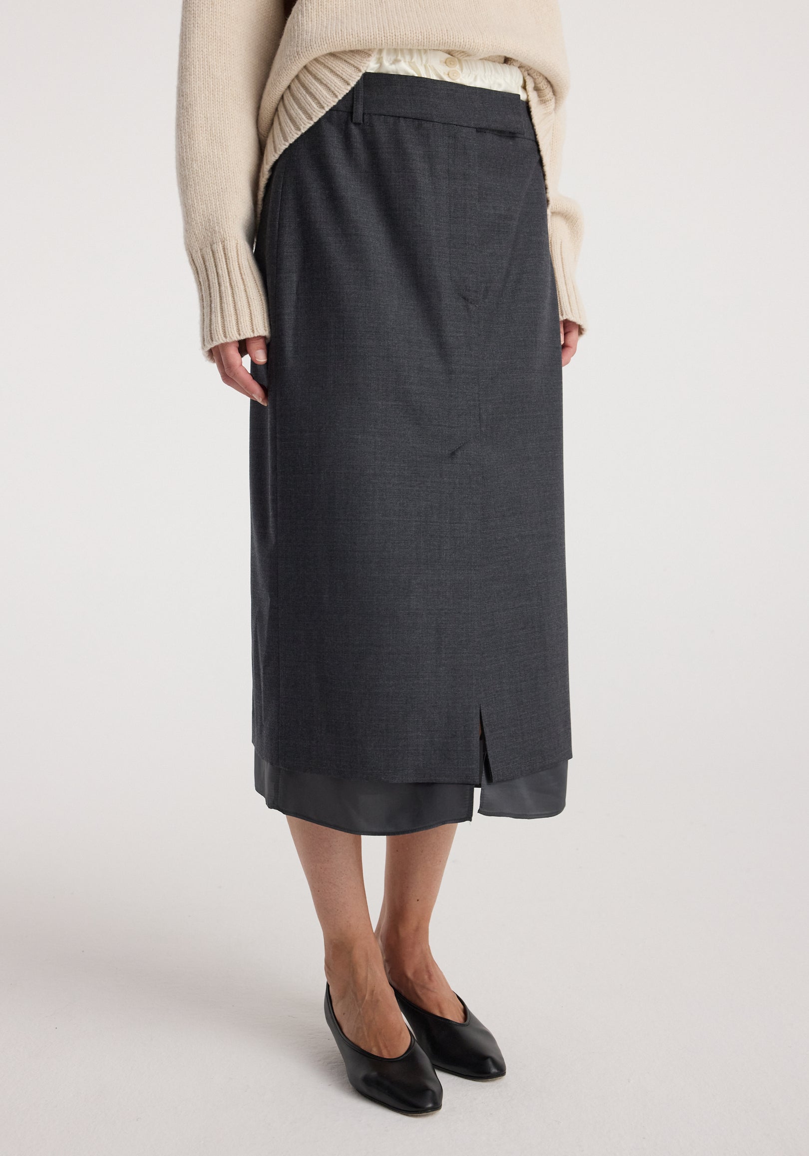 Woman wearing a layered dark grey melange skirt with a subtle front slit and a soft beige sweater, paired with black pointed-toe flats, Boxer detailed skirt | dark grey melange.