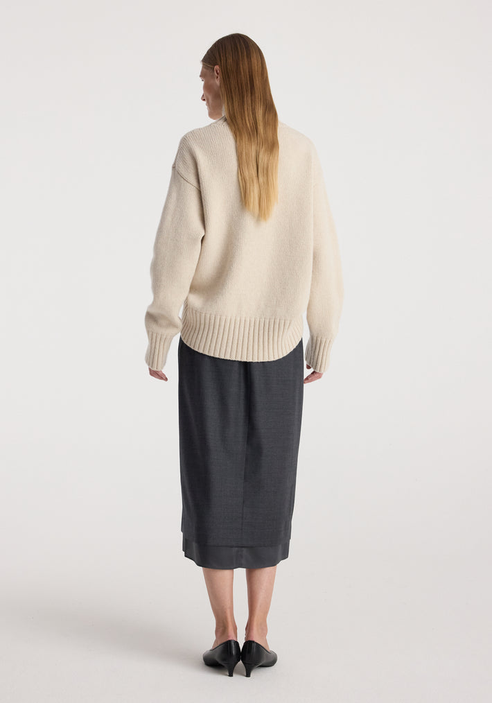 Rear view of a woman wearing a cream textured sweater paired with a dark grey melange Boxer detailed skirt | dark grey melange, standing against a plain white background.