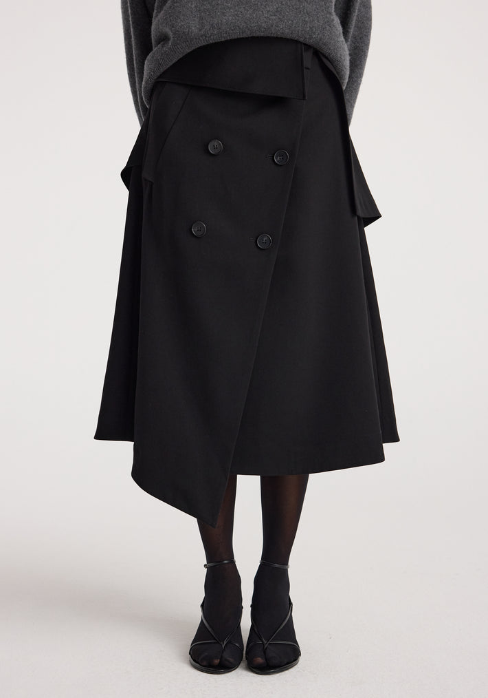 Woman wearing a black Deconstructed trench skirt | black with asymmetrical hem and double-breasted button detail paired with black tights and open-toe heels.
