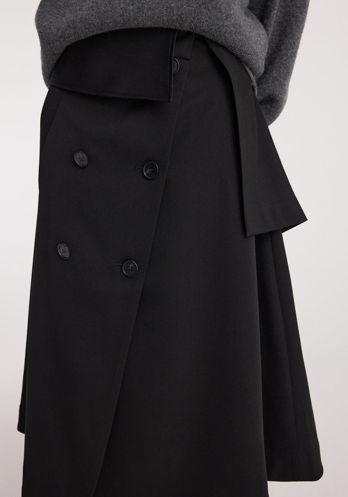 Close-up of a black Deconstructed trench skirt | black featuring an asymmetrical wrap design with button details, worn with a gray sweater.