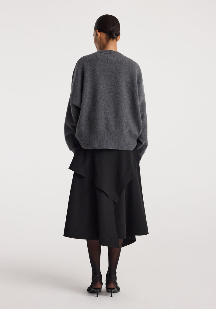Woman wearing a loose grey sweater paired with a layered black skirt viewed from the back, showcasing the Deconstructed trench skirt | black with an asymmetrical hemline.