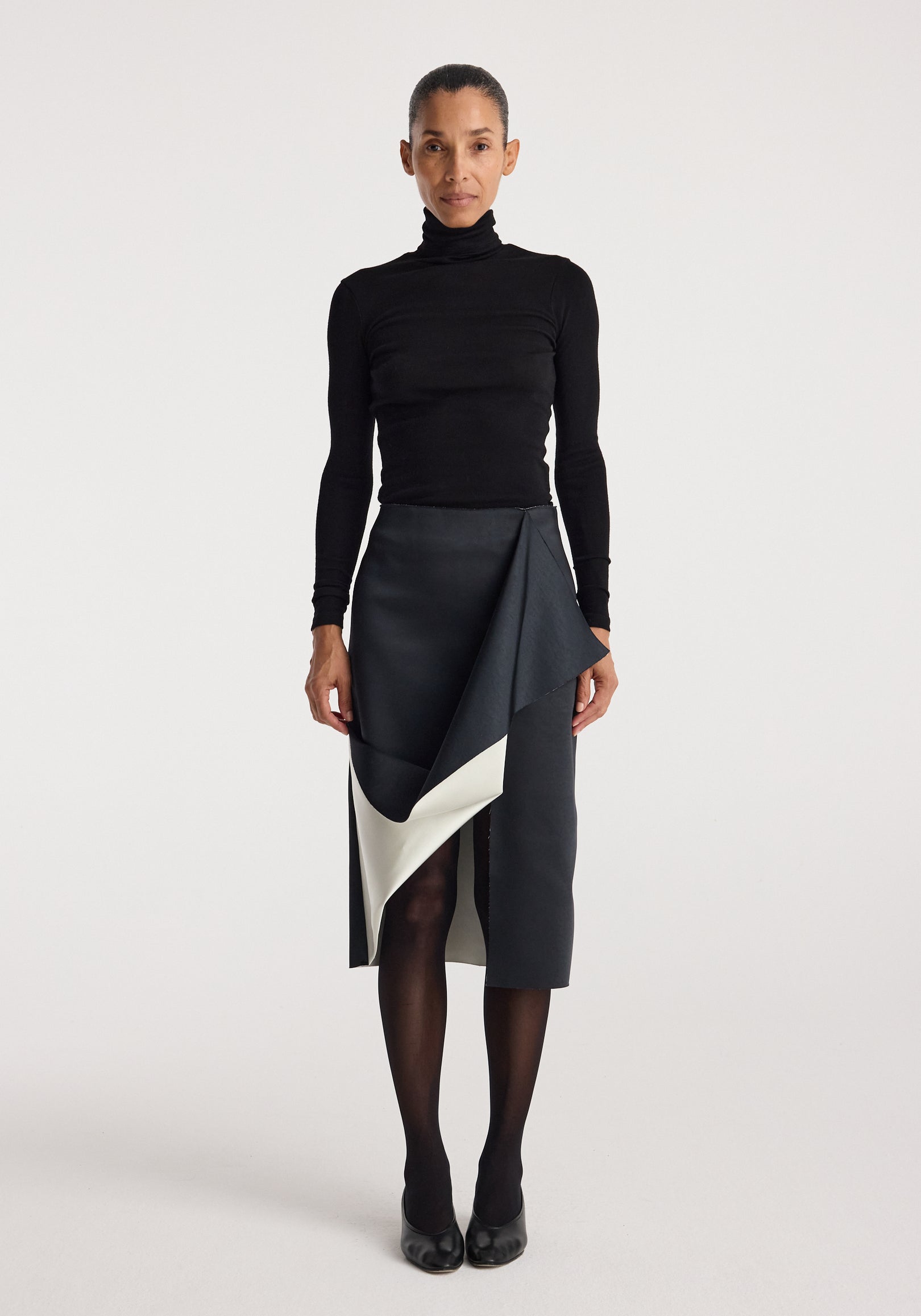 Woman wearing a black turtleneck top paired with a Sculptural double-satin skirt | black/white featuring a folded, asymmetrical design and a contrasting white inner layer.