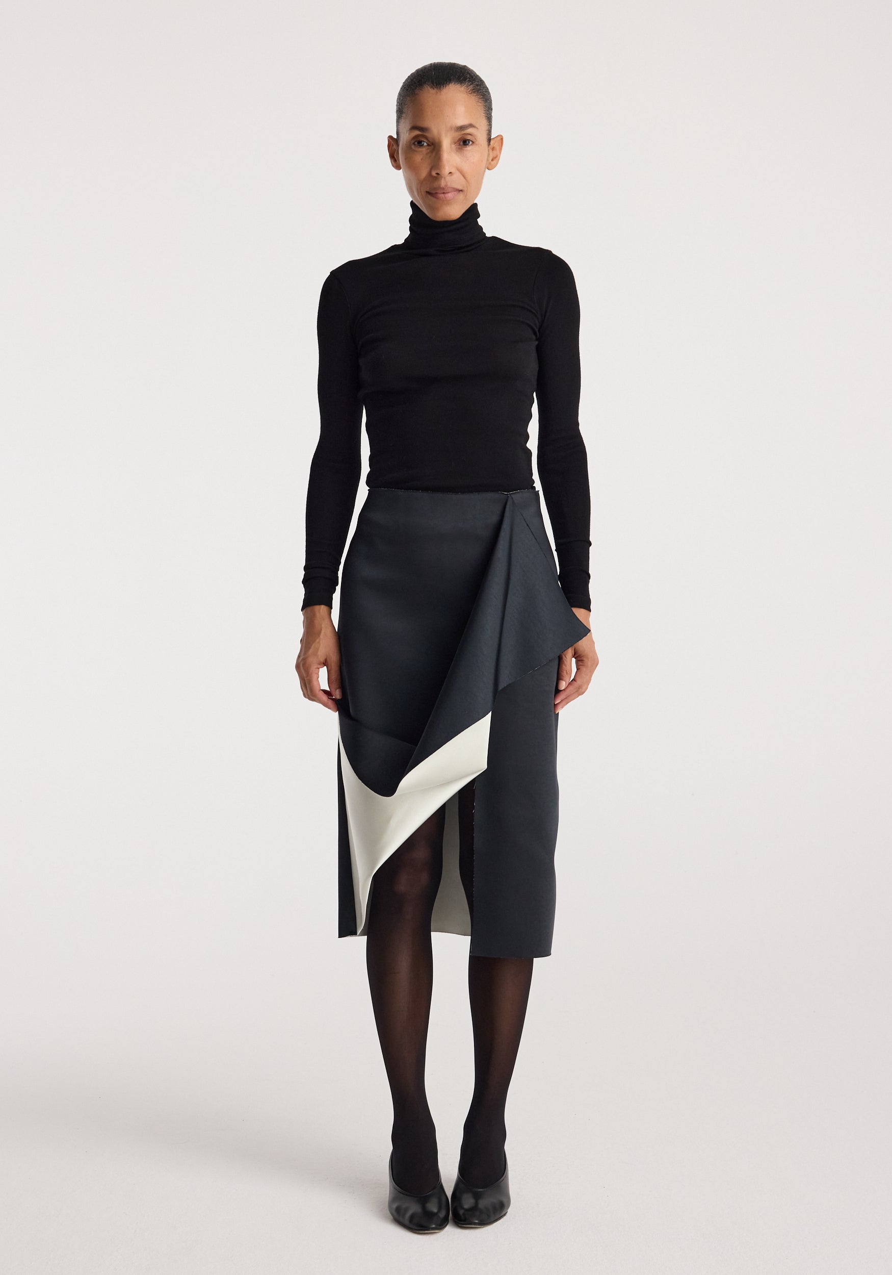 Woman wearing a black turtleneck top paired with a Sculptural double-satin skirt | black/white featuring a folded, asymmetrical design and a contrasting white inner layer.