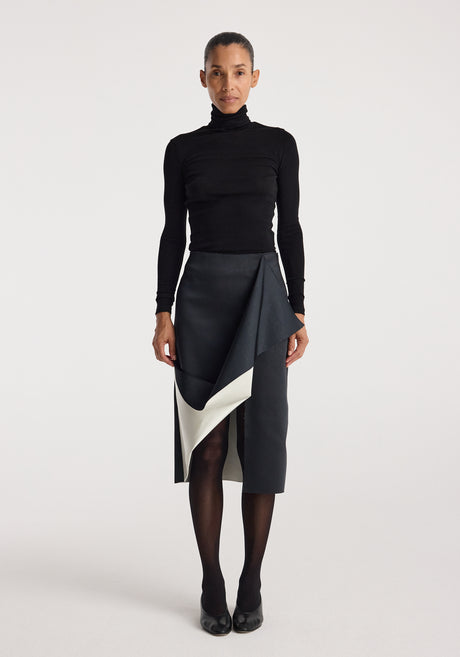 Woman wearing a black turtleneck top paired with a Sculptural double-satin skirt | black/white featuring a folded, asymmetrical design and a contrasting white inner layer.