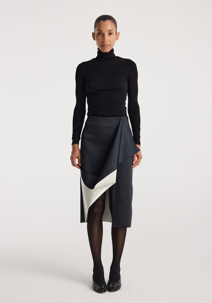 Woman wearing a black turtleneck top paired with a Sculptural double-satin skirt | black/white featuring a folded, asymmetrical design and a contrasting white inner layer.