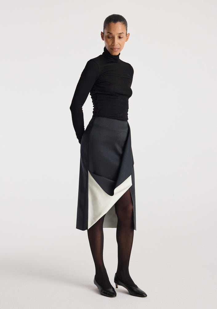 Woman wearing a black turtleneck top paired with a Sculptural double-satin skirt | black/white featuring a folded, asymmetrical design and a contrasting white inner layer.