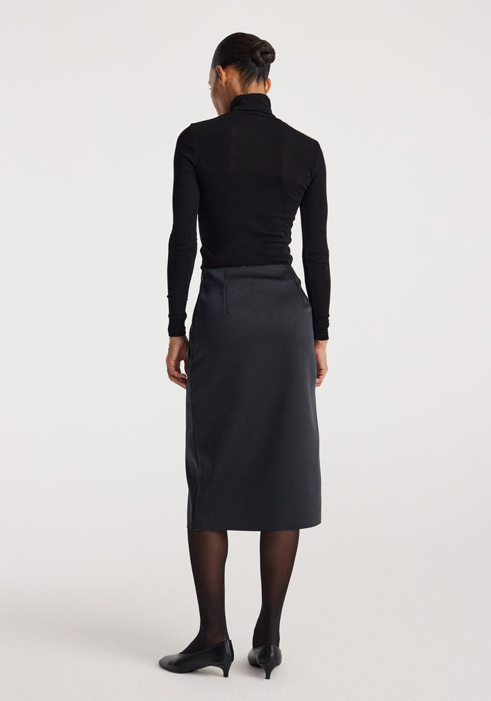 Woman wearing a black long-sleeve top and black heels, viewed from the back, showcasing the sculptural double-satin skirt | black/white with a midi length and sleek fit.