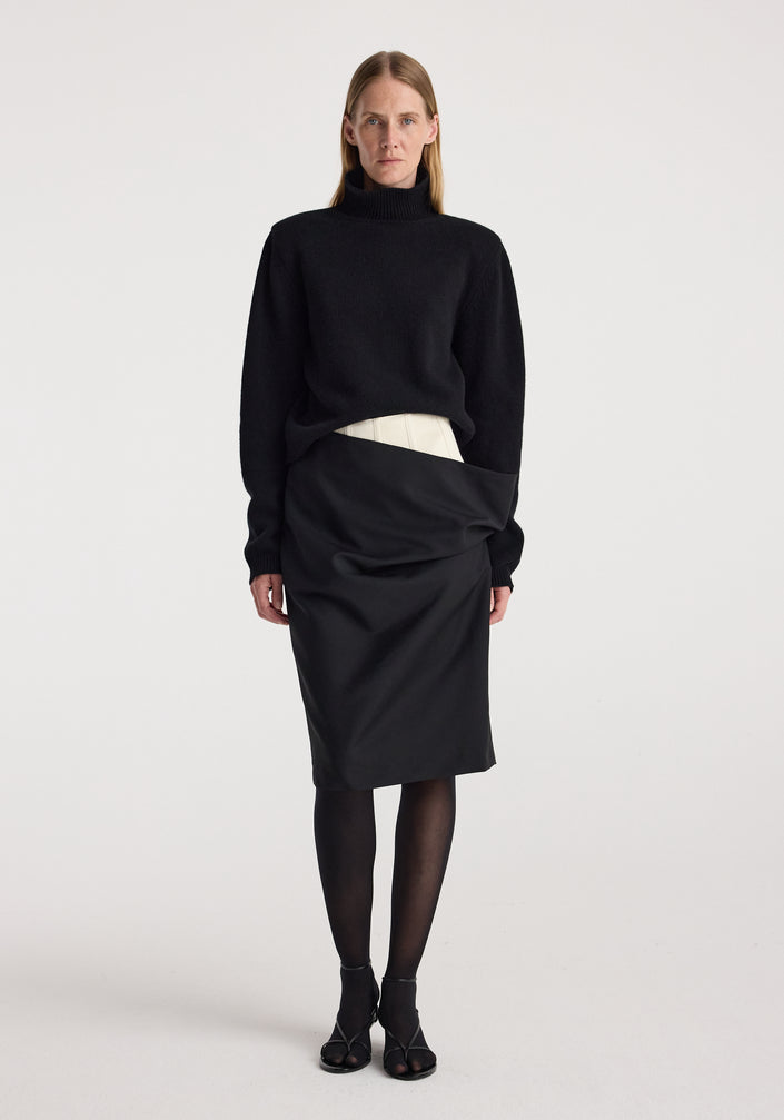 Model wearing a Double waistband skirt | black paired with a black long-sleeve turtleneck sweater, black sheer tights, and black open-toe heels against a plain white background.