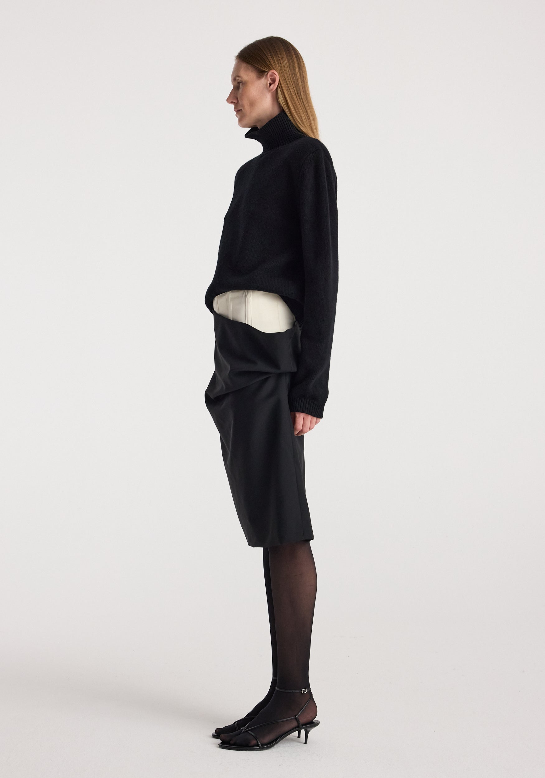 Woman wearing black turtleneck sweater and black sheer tights paired with the Double waistband skirt | black, featuring a unique double waistband design and knee-length fit.