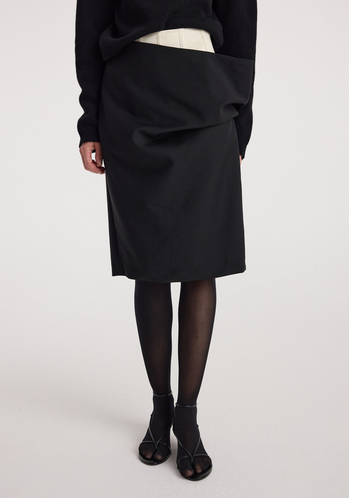 Woman wearing a black Double waistband skirt | black with a unique double waistband design, paired with black tights and open-toe black heels.