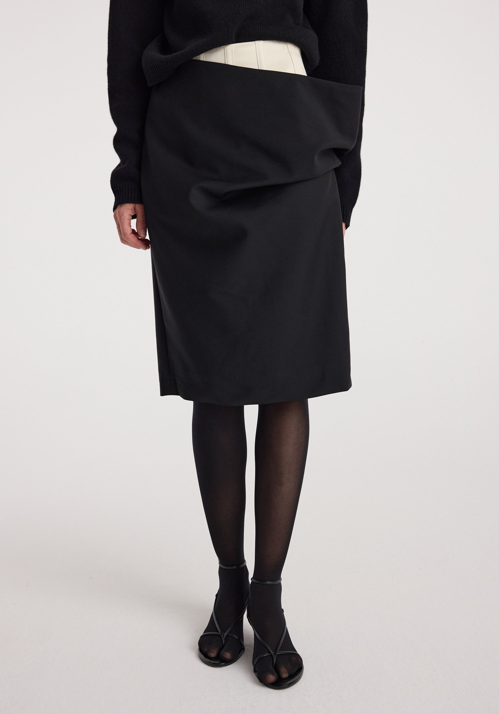 Woman wearing a black Double waistband skirt | black with a unique double waistband design, paired with black tights and open-toe black heels.