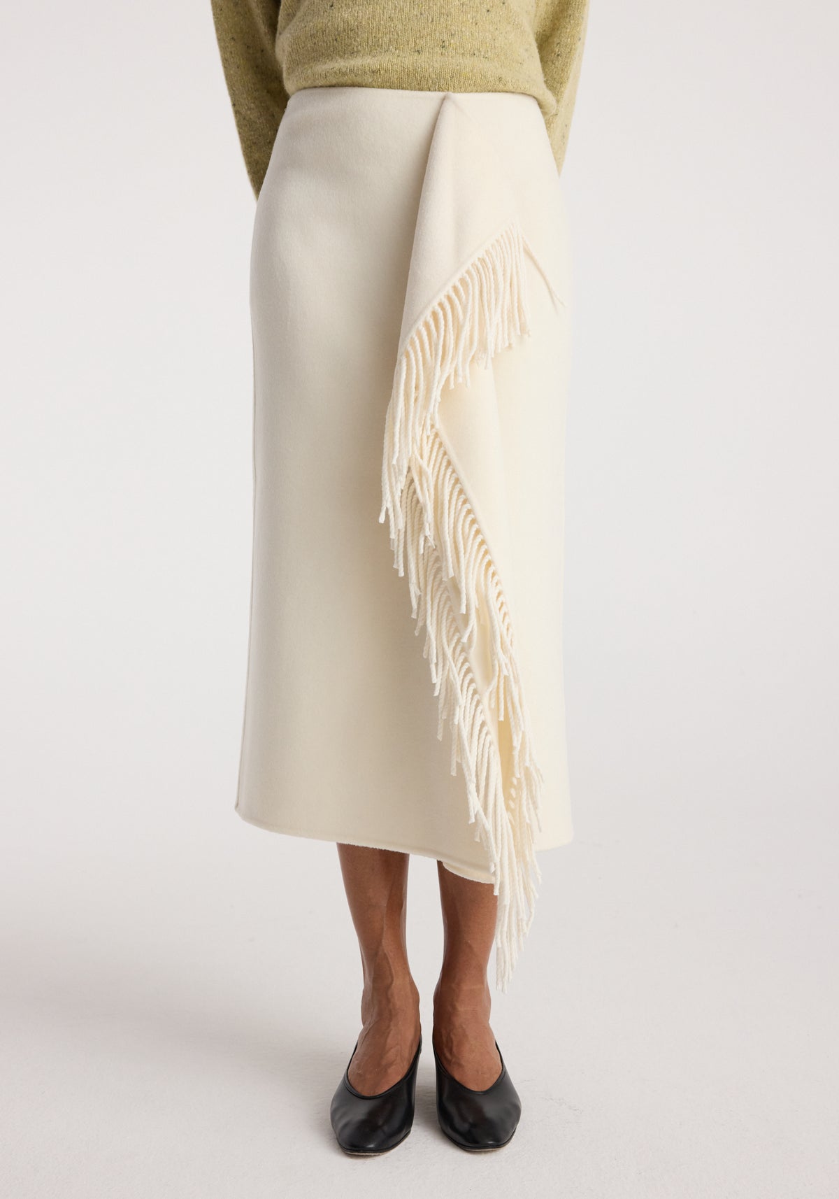 Woman wearing an off white Double-faced fringe skirt | off white featuring a straight cut and long fringe detail cascading down one side, paired with black shoes.