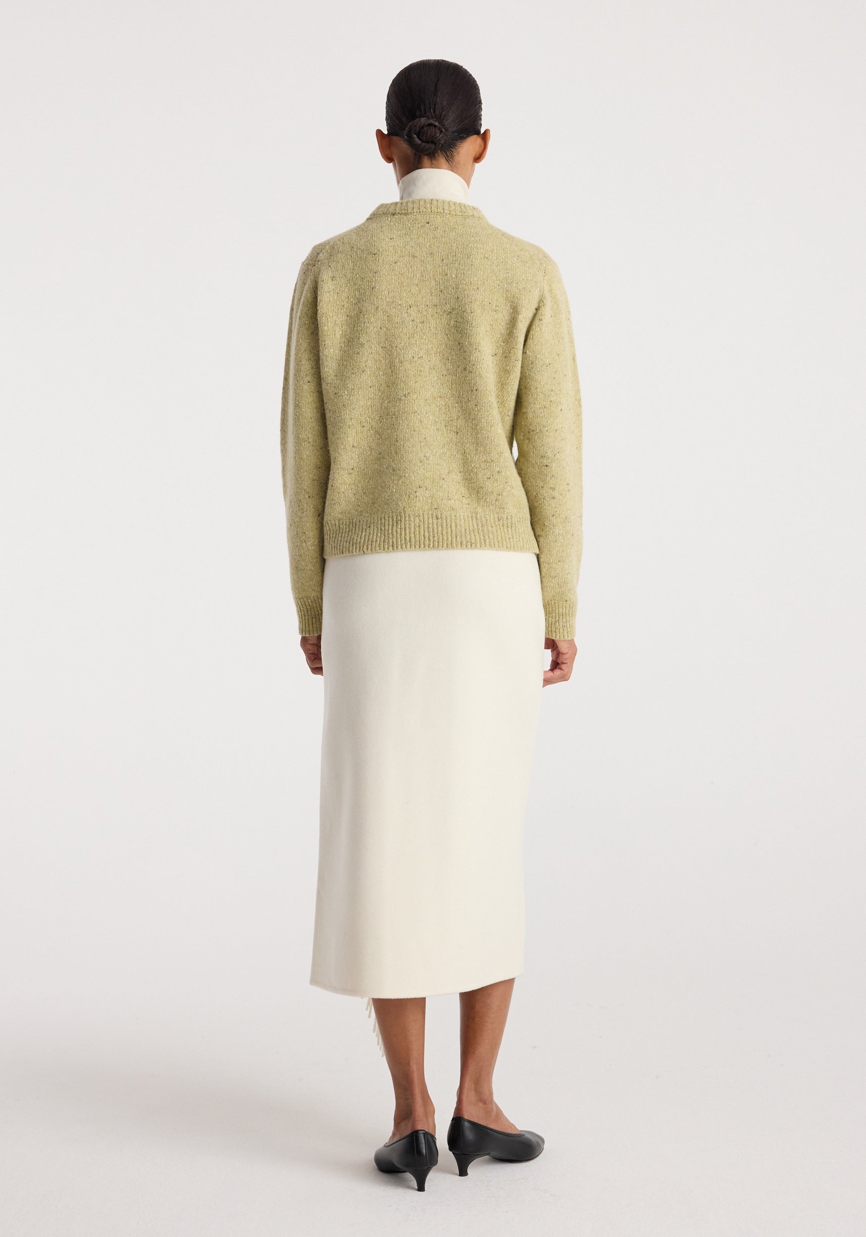Woman wearing a beige knitted sweater paired with a long off white Double-faced fringe skirt | off white and black low-heeled shoes, shown from the back.