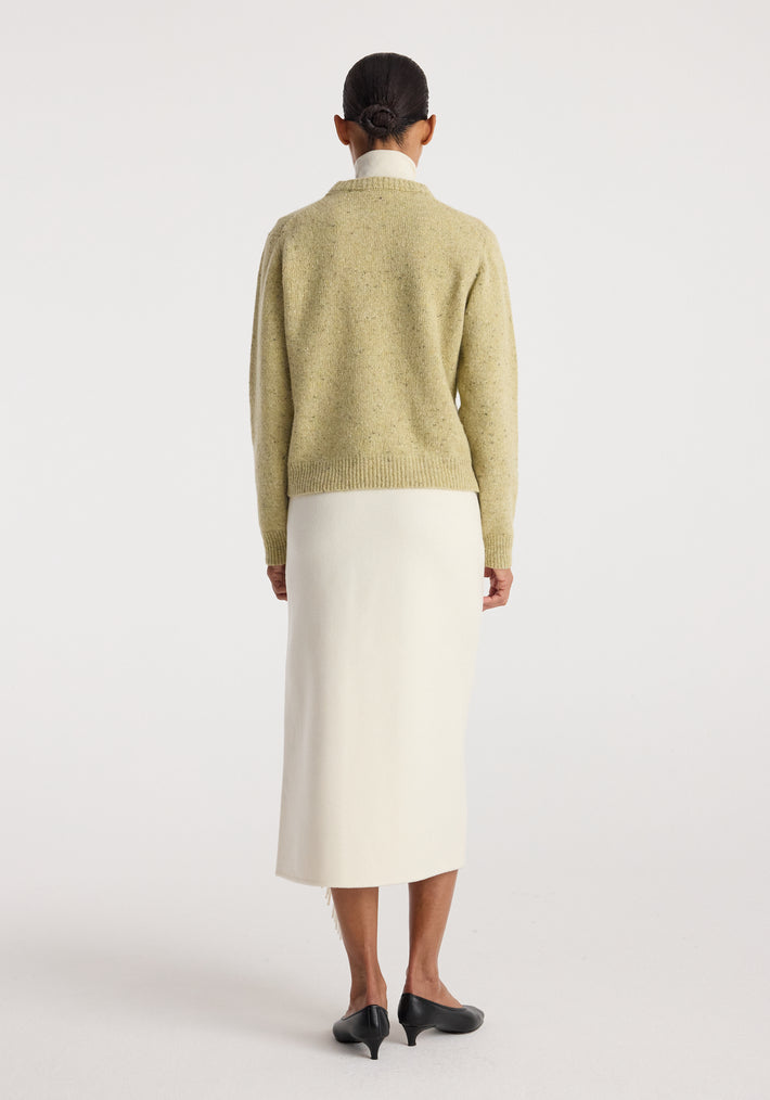 Woman wearing a beige knitted sweater paired with a long off white Double-faced fringe skirt | off white and black low-heeled shoes, shown from the back.