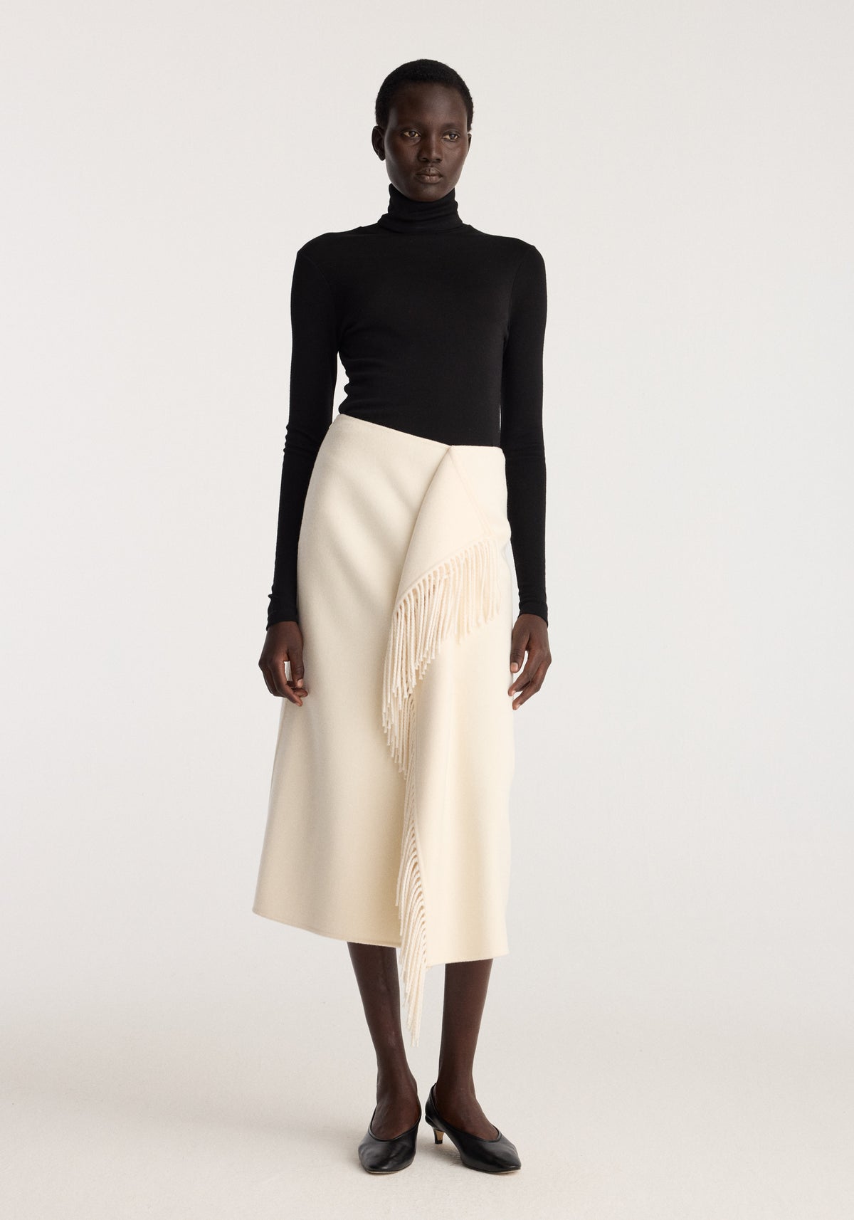 Double-faced fringe skirt | off white shown on a model with an asymmetrical wrap front and long fringe detail styled with a black turtleneck outfit