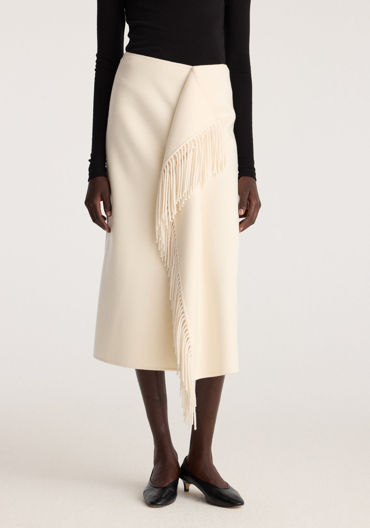Double-faced fringe skirt | off white styled with a black long sleeve top and flats featuring an asymmetrical wrap front and long fringe detail