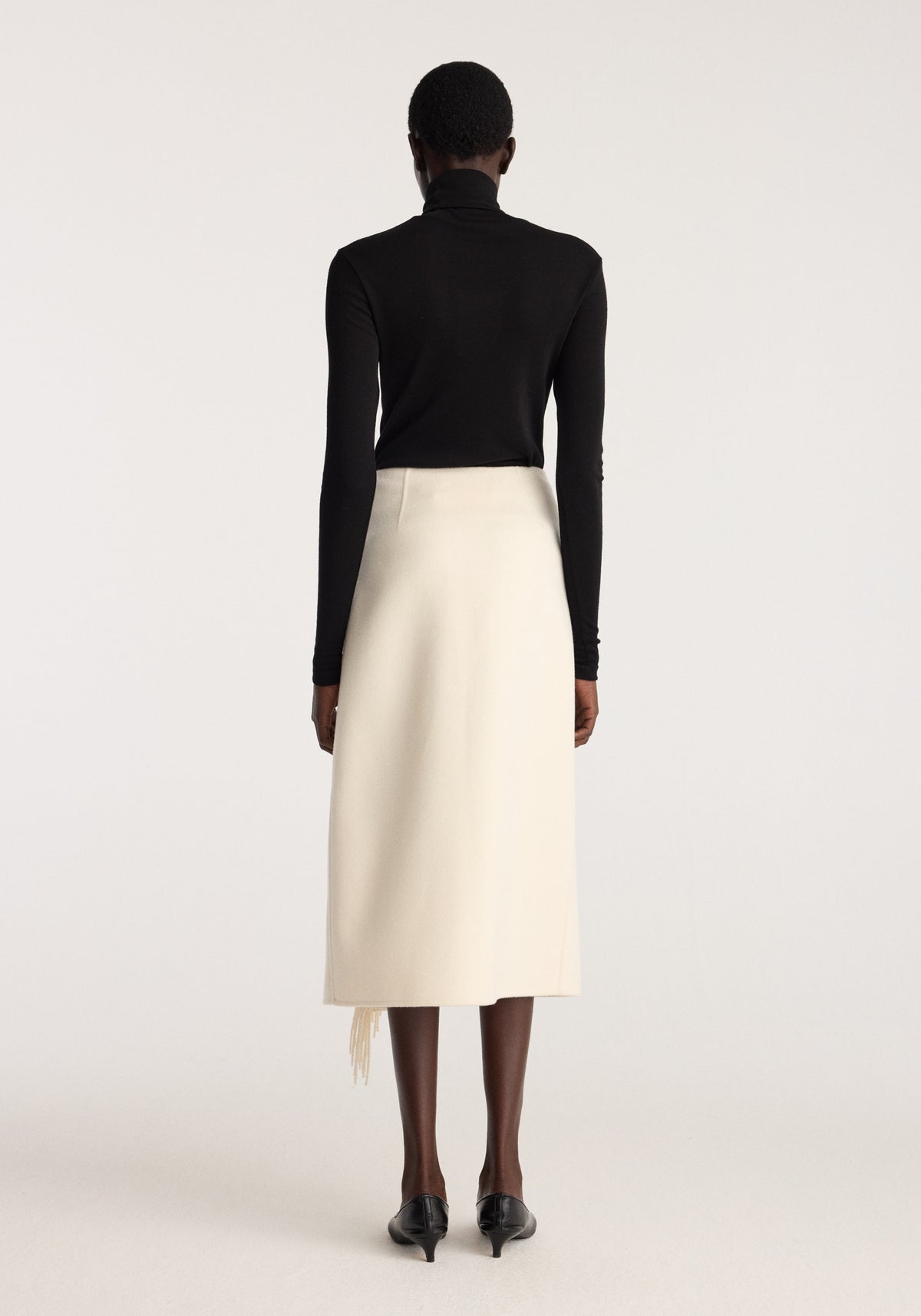 Double-faced fringe skirt | off white shown from the back on a model with a black fitted top and pointed shoes and fringe detail peeking from the hem