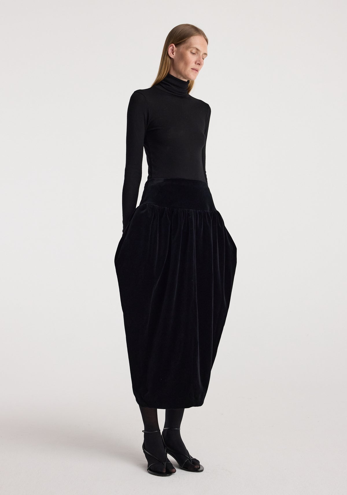 Model wearing Sculptural volume velvet skirt | black, featuring a dramatic rounded silhouette and gathered velvet texture with a fitted black top and ankle boots