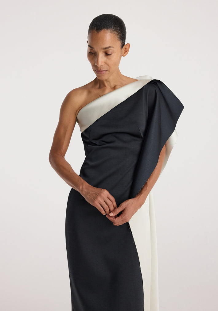 Woman wearing sculptural double-satin off-shoulder dress | black/white with an asymmetrical neckline and draped design against a plain light background.