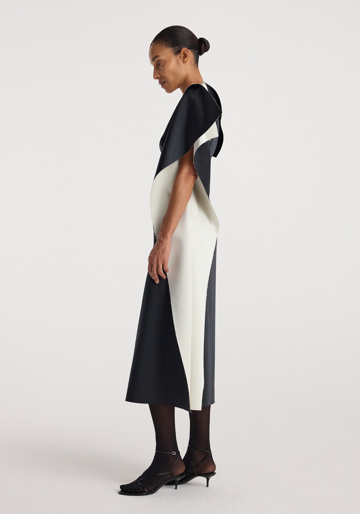 Model wearing sculptural double-satin off-shoulder dress | black/white with a sleek silhouette and asymmetrical color block design against a plain background.