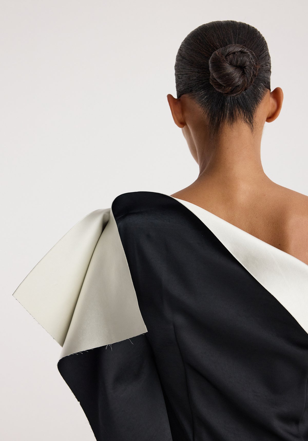 Rear view of a model wearing a Sculptural double-satin off-shoulder dress | black/white featuring a bold, structured design with contrasting black and white panels and an elegant off-shoulder silhouette.