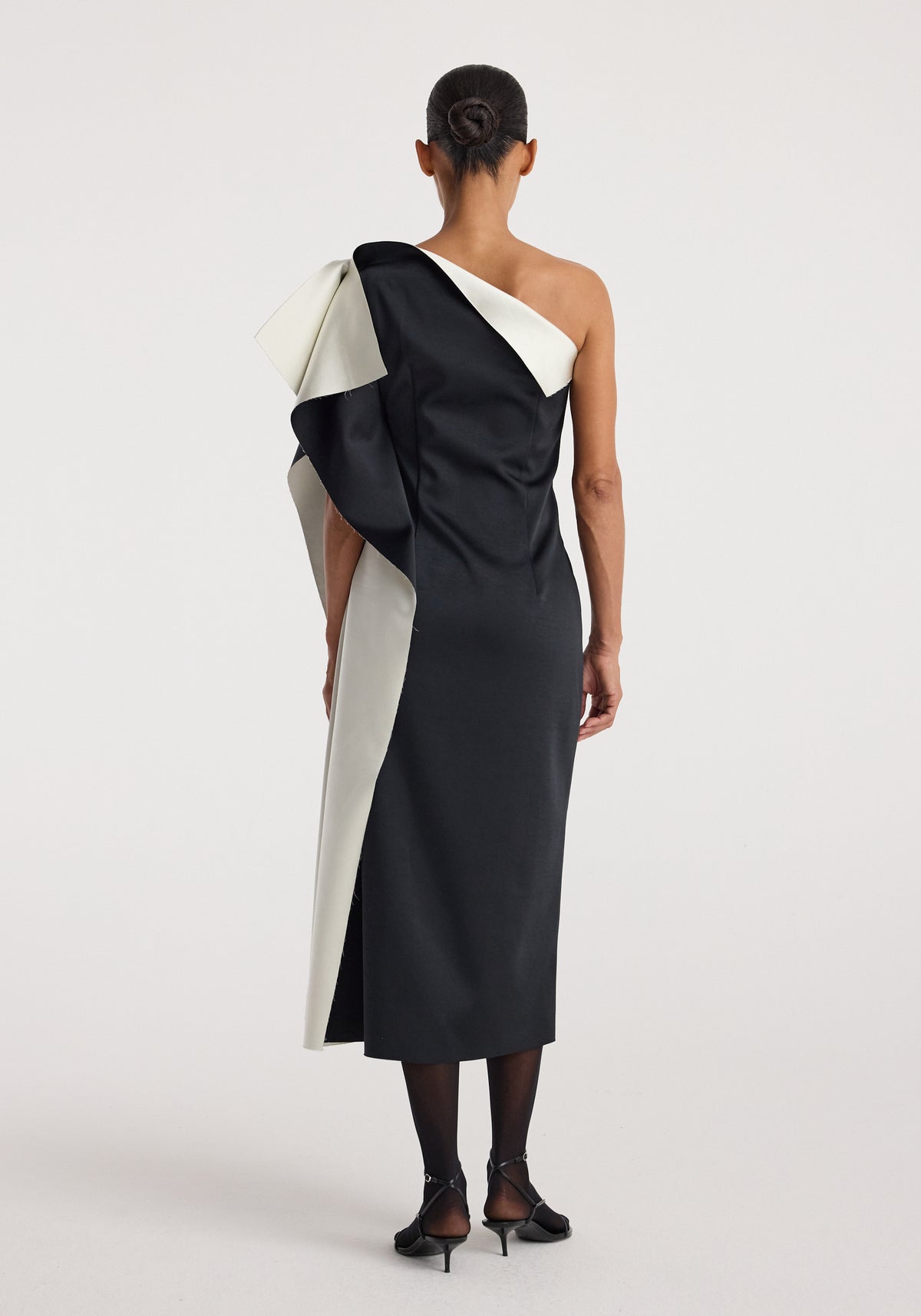 Woman wearing a sculptural double-satin off-shoulder dress | black/white with a dramatic asymmetric design and a fitted silhouette viewed from the back.