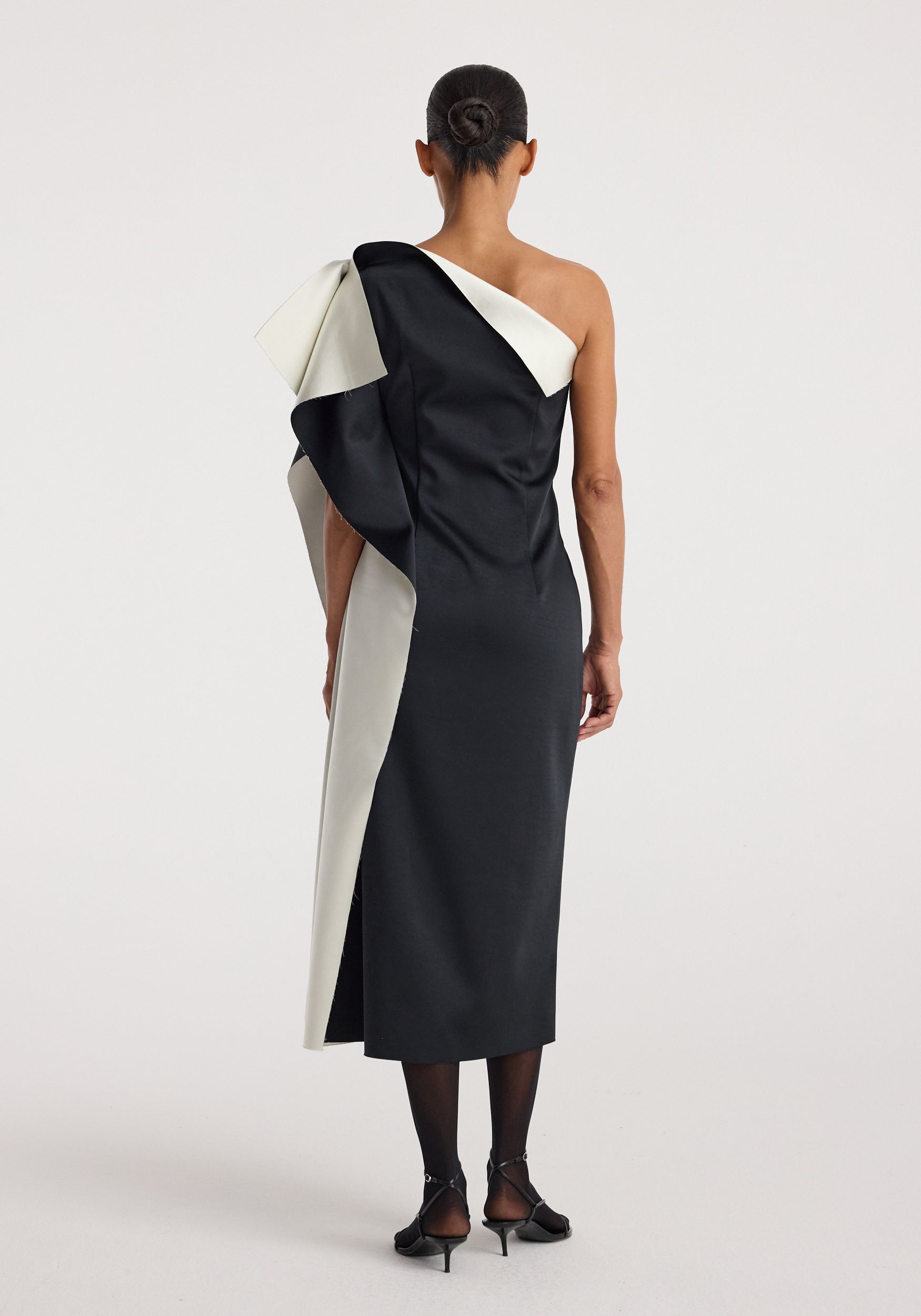 Woman wearing a sculptural double-satin off-shoulder dress | black/white with a dramatic asymmetric design and a fitted silhouette viewed from the back.
