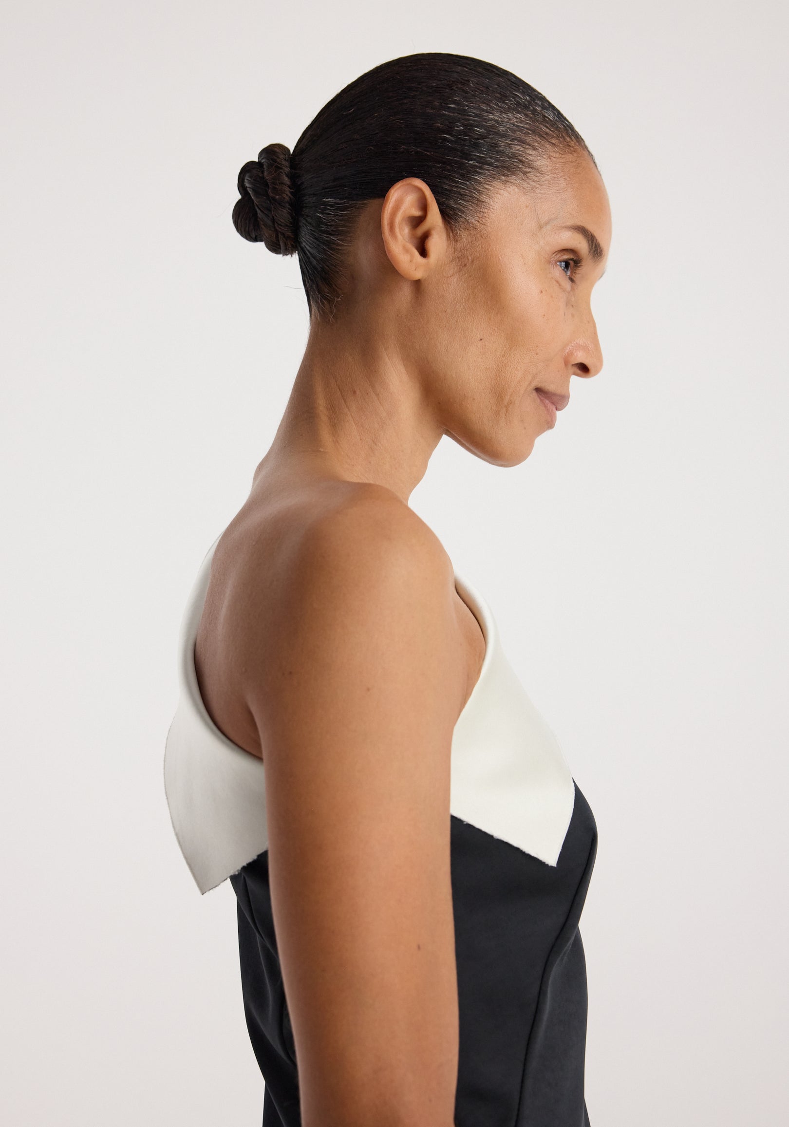 Profile view of a woman wearing a sculptural double-satin off-shoulder dress | black/white, highlighting the elegant off-shoulder neckline and smooth satin fabric.
