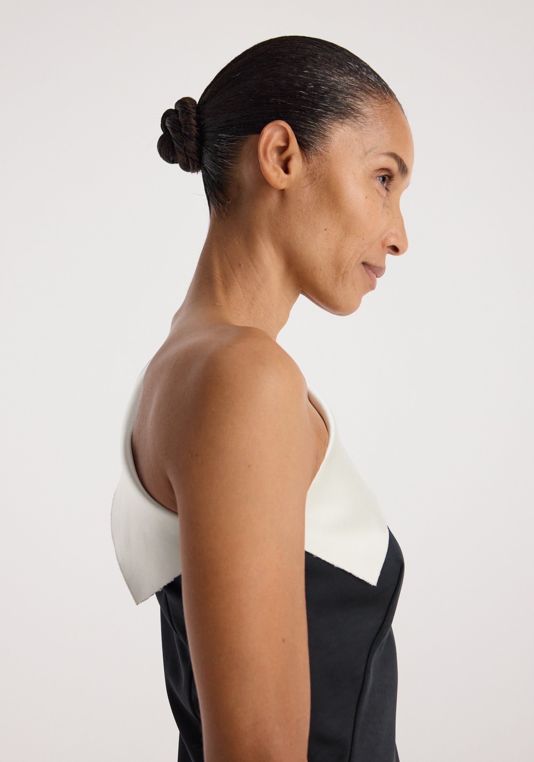 Profile view of a woman wearing a sculptural double-satin off-shoulder dress | black/white, highlighting the elegant off-shoulder neckline and smooth satin fabric.