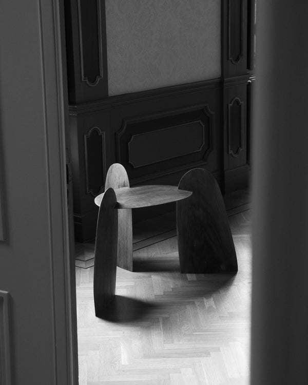 Sculpted Stool | 4673, handcrafted from oak, features three interlocking curved panels supporting a round top, set on a herringbone-patterned hardwood floor.