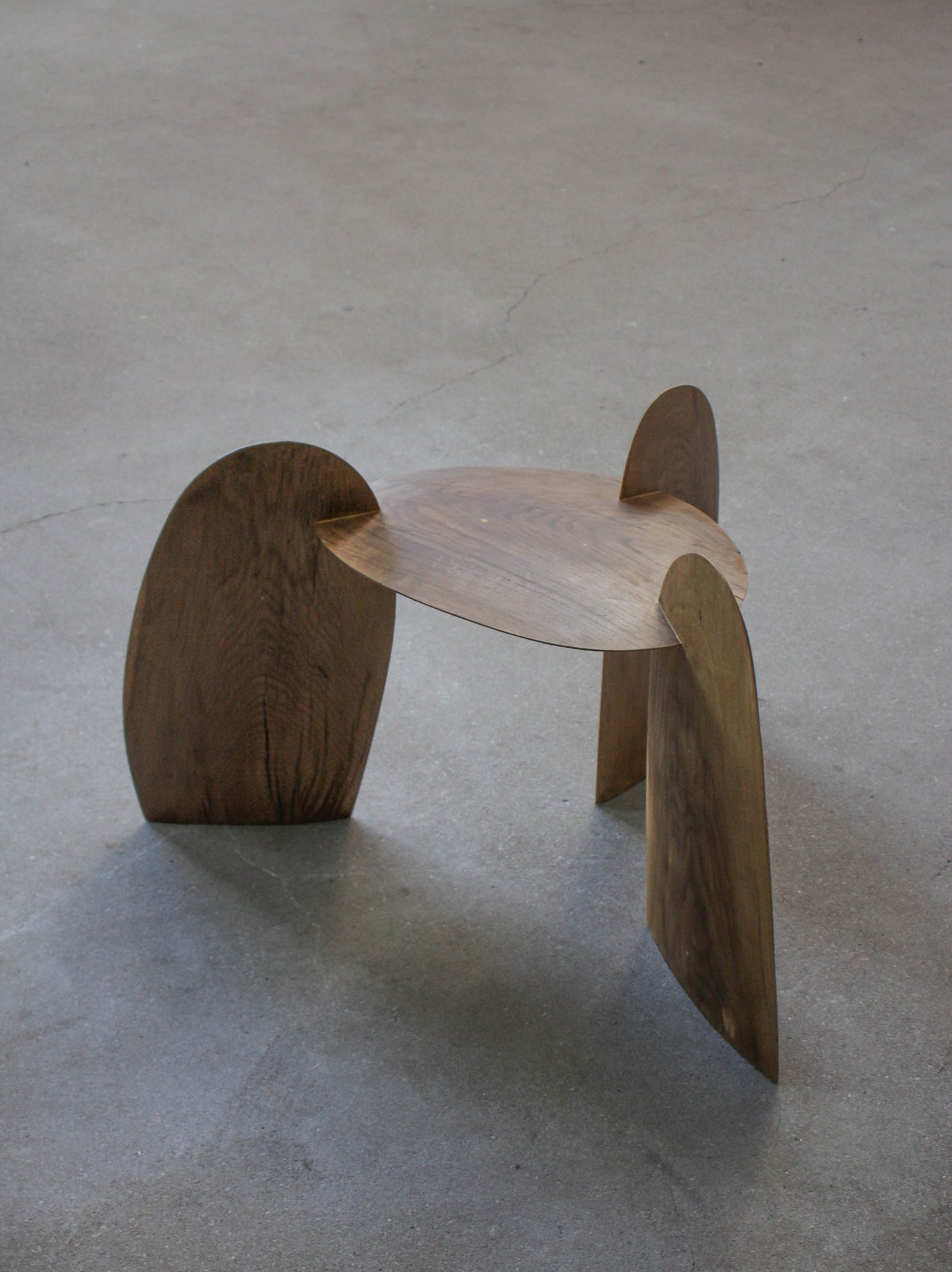 Sculpted Stool | 4673: A handcrafted, interlocking oak stool by Arne Kristian, featuring a minimalist tripod design, displayed on a concrete floor.