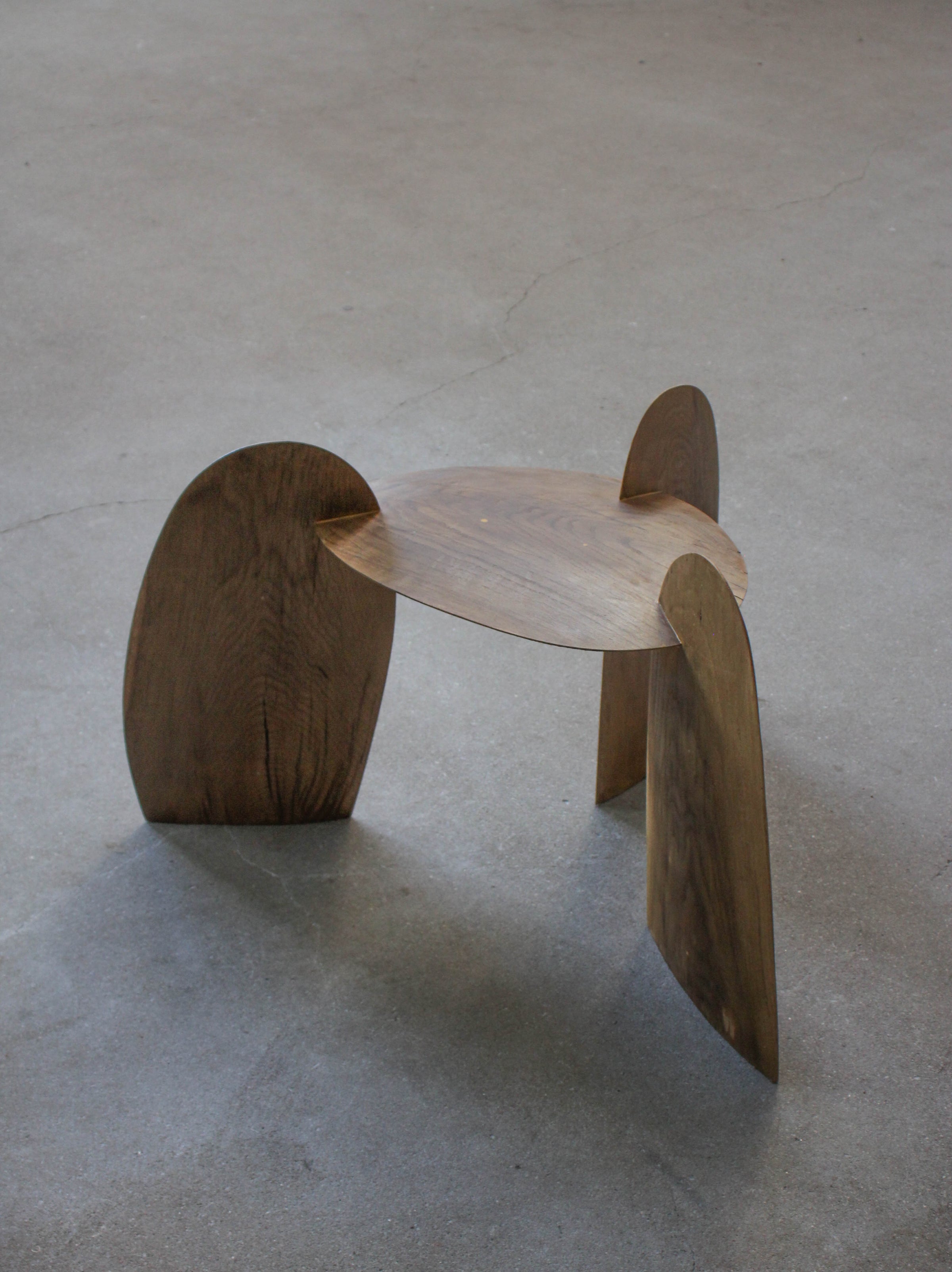 Sculpted Stool | 4673: A handcrafted, interlocking oak stool by Arne Kristian, featuring a minimalist tripod design, displayed on a concrete floor.
