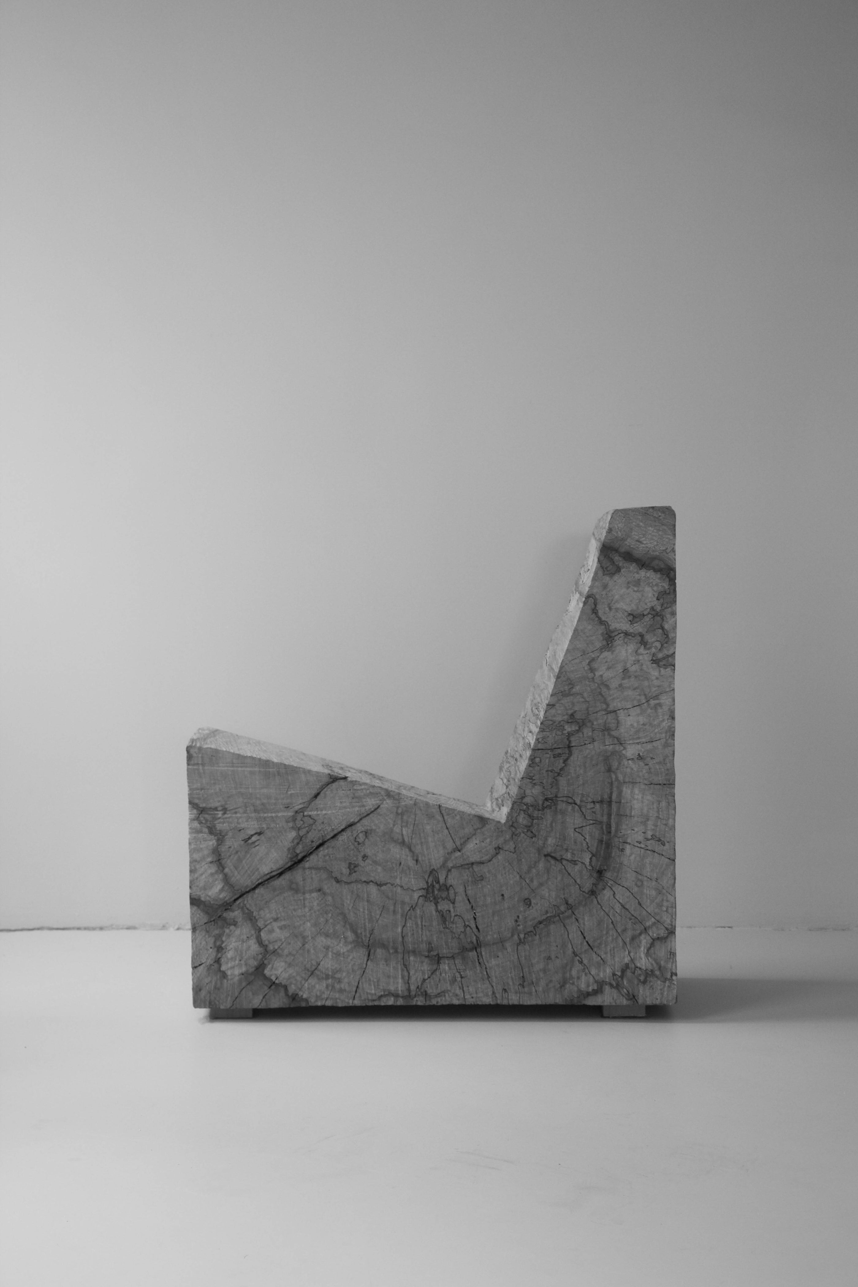 Side view of a modern chair carved from a solid block of rough, natural stone with angular lines and a textured surface, named Brutalist Chair | 5788.