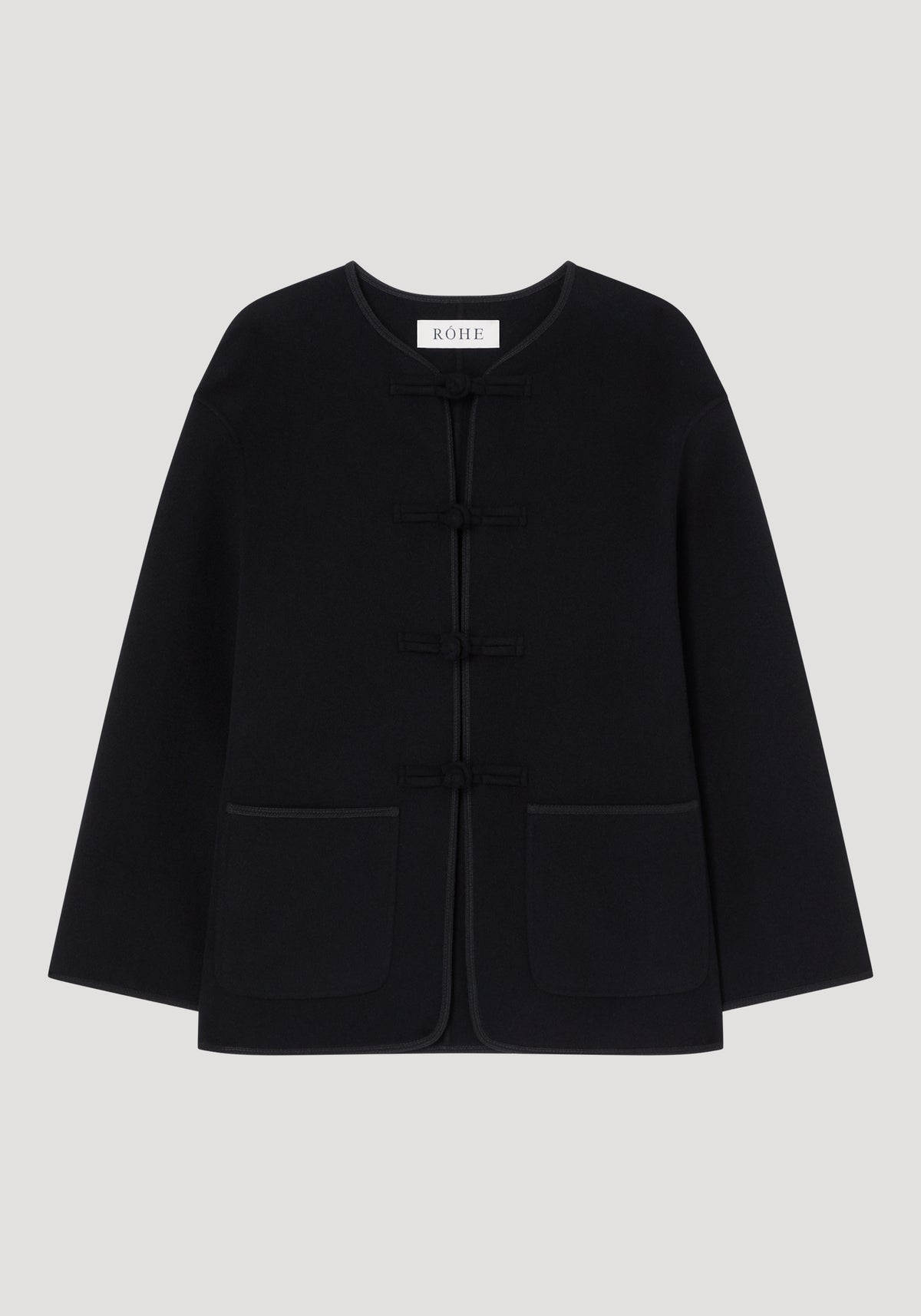 Mandarin double-faced wool jacket in black with frog fastenings, round neckline, long sleeves, patch pockets, and embroidered edges; labeled “RÓHE” at the neckline.