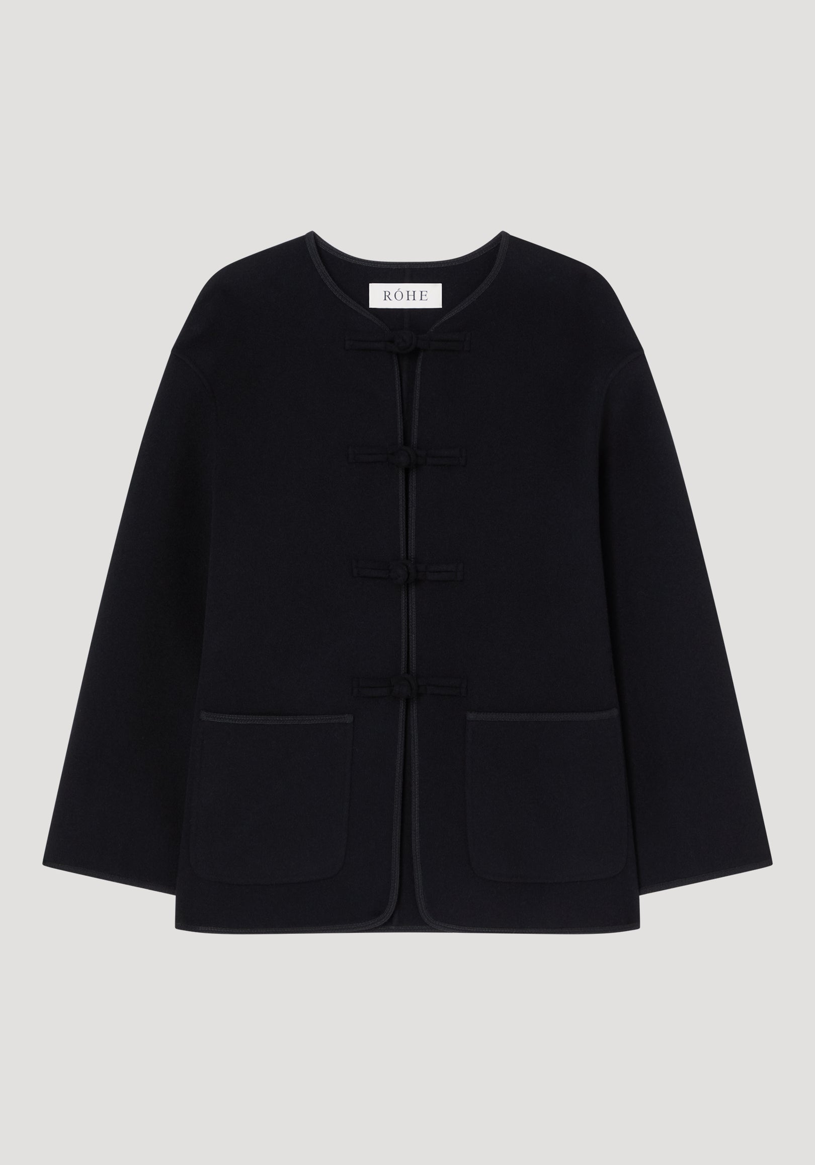 Mandarin double-faced wool jacket in black with frog fastenings, round neckline, long sleeves, patch pockets, and embroidered edges; labeled “RÓHE” at the neckline.