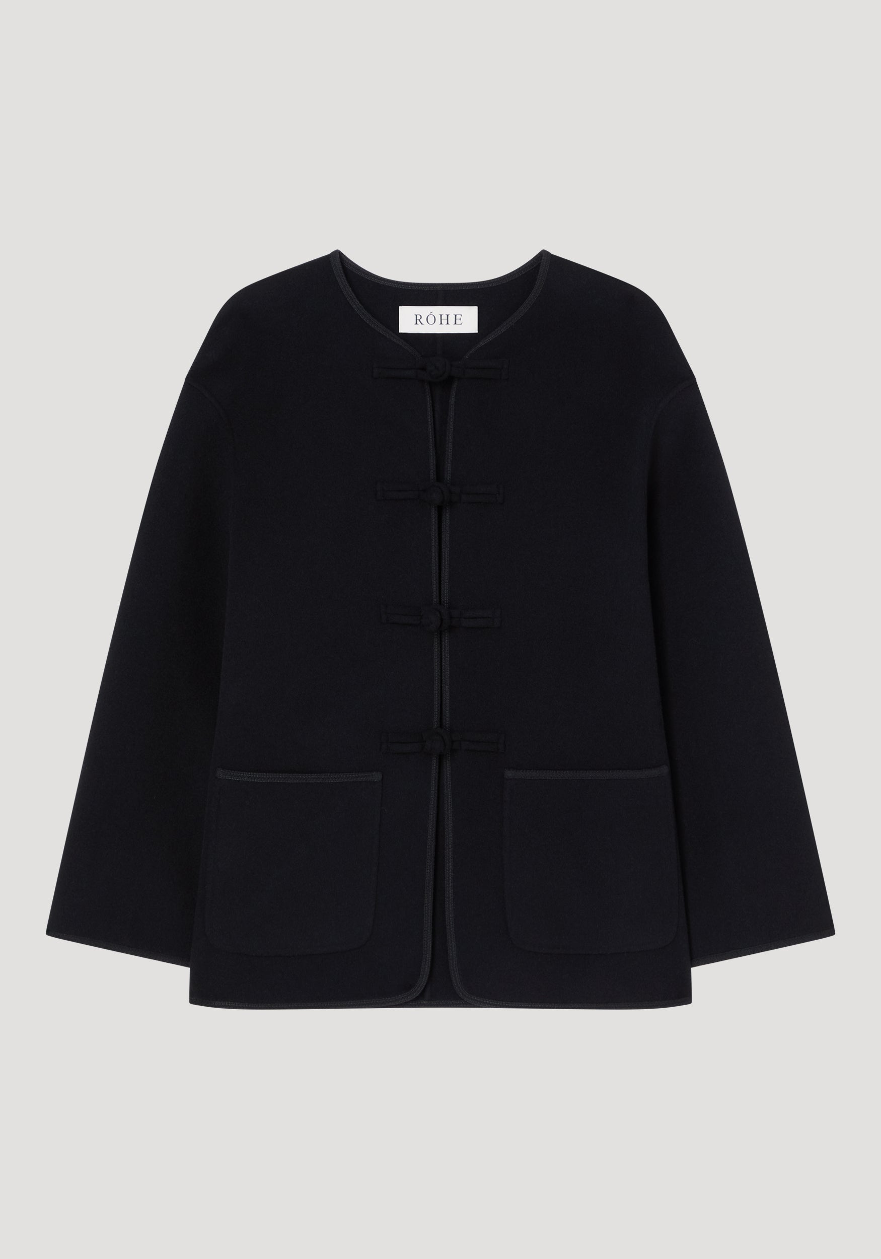 Mandarin double-faced wool jacket in black with frog fastenings, round neckline, long sleeves, patch pockets, and embroidered edges; labeled “RÓHE” at the neckline.