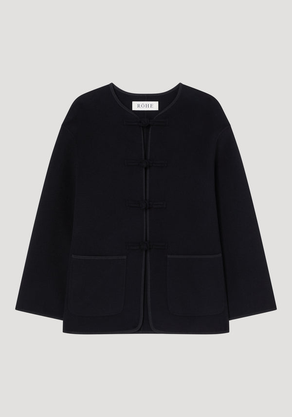 Mandarin double-faced wool jacket in black with frog fastenings, round neckline, long sleeves, patch pockets, and embroidered edges; labeled “RÓHE” at the neckline.