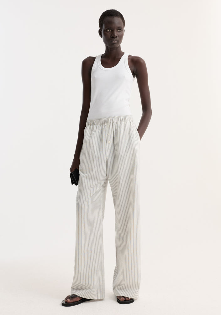 Model in Silk stripe pyjama trousers | fine stripe, featuring wide-leg design and elasticated waistband, paired with a white rib-tank and black sandals.