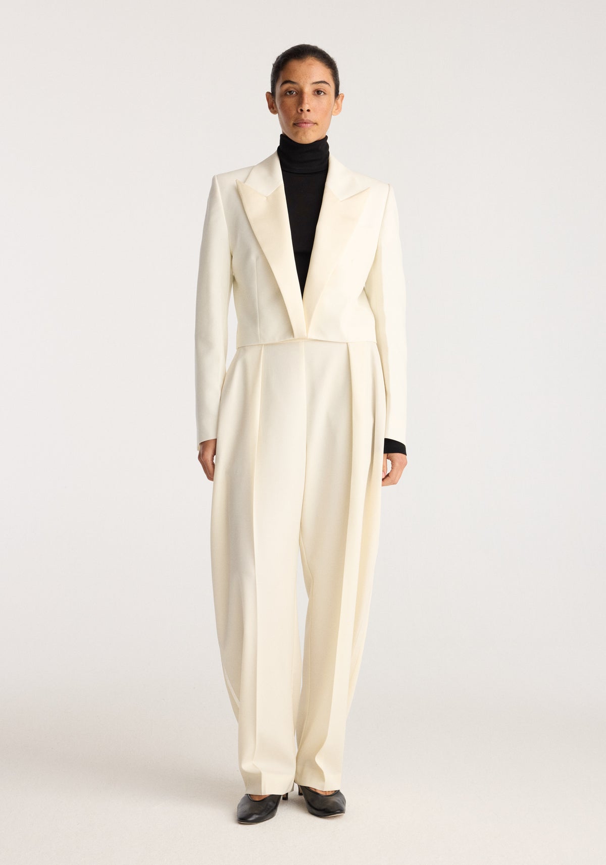 Cropped blazer | off white worn by a model with a tailored fit and peaked lapels over a black turtleneck in a studio setting