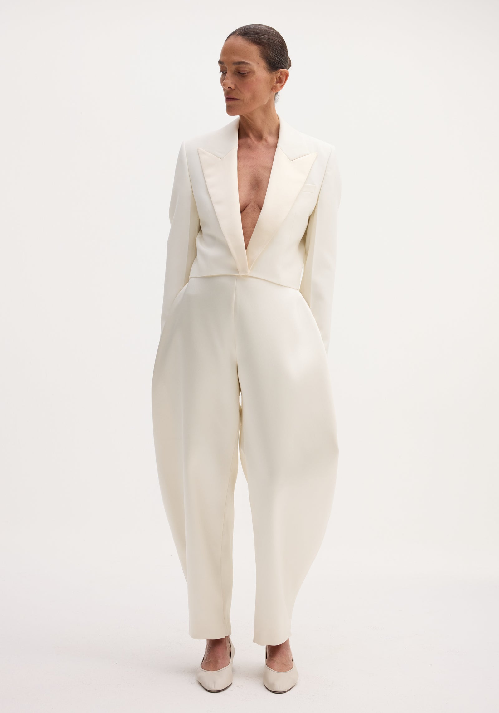 Model wearing Cropped blazer | off white, featuring contrasting satin lapels, a deep V-neck, and high-waisted trousers, creating a sophisticated, tailored look.